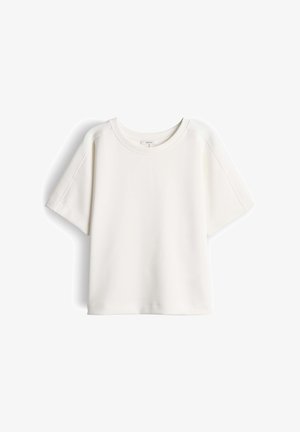 Witte T-shirt met korte mouwen en losse pasvorm, ronde halslijn, zichtbare naadtoeslagen op de mouwen en schouders, getoond tegen een effen achtergrond.