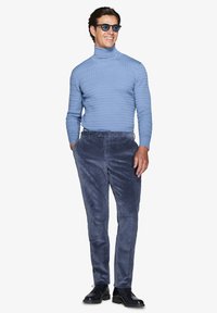 Lyseblå struktur sweater med høj hals kombineret med mørkeblå flannelsbukser og sorte sko, hvilket skaber et sammenhængende outfit.