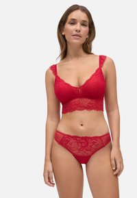 Bralette de encaje rojo con bordes de ondas y tirantes con volantes, combinado con braguitas hipster de encaje rojo a juego con patrones florales.