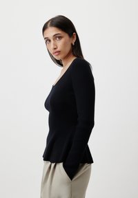Black long-sleeve ribbed top with a fitted design and scoop neckline, featuring a flared hem, paired with beige trousers.