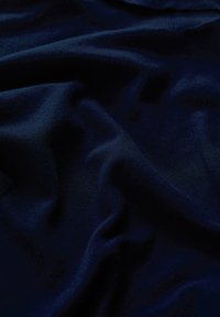 Tumši zils audums ar mīkstu, teksturētu virsmu, demonstrējot maigas krokas un viļņus, kas norāda uz vieglu un gludu materiālu.