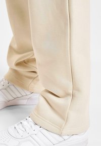 Beige bomulds-sweatpants med en afslappet pasform, der har lige ben og en glat tekstur, parret med hvide sneakers med striber.