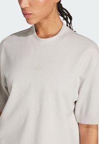 Top de manga corta de color gris claro hecho de tela texturizada. Presenta un cuello alto y un pequeño logo en relieve en el pecho.