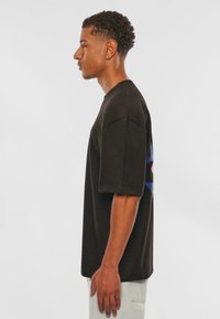 Sort kortærmet t-shirt med løs pasform, der har et farverigt grafisk design på ryggen og en rund halsudskæring.