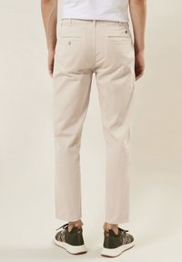 Licht beige broek met een slim fit, voorzien van vier zakken, nette stiksels en een zachte textuur. Gepaard met donker groene sportschoenen.