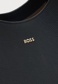 Mustast tekstureeritud nahapinnast, mille lähedal õmmeldud serva ääres on kinnitatud väikesed kuldsed metalltähed, mis moodustavad sõna "BOSS".