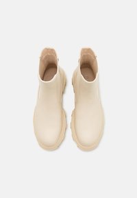 Beige nahkasaappaat nilkkamittaisilla joustavilla paneeleilla, pyöreällä kärjellä ja kumipohjalla. Sileä pinta, jossa on minimaalista ommeltu sisustus.