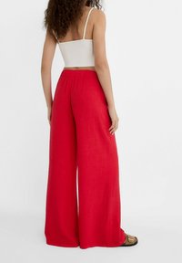 Rote weit geschnittene Hose aus strukturiertem Stoff mit elastischem Bund. Kombiniert mit einem weißen, taillierten Crop-Top, das ein lässiges Outfit zeigt.