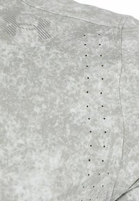 Maglietta sportiva grigio chiaro con motivo testurizzato e screziato, piccoli fori lungo il lato e un logo del marchio discreto sul davanti.