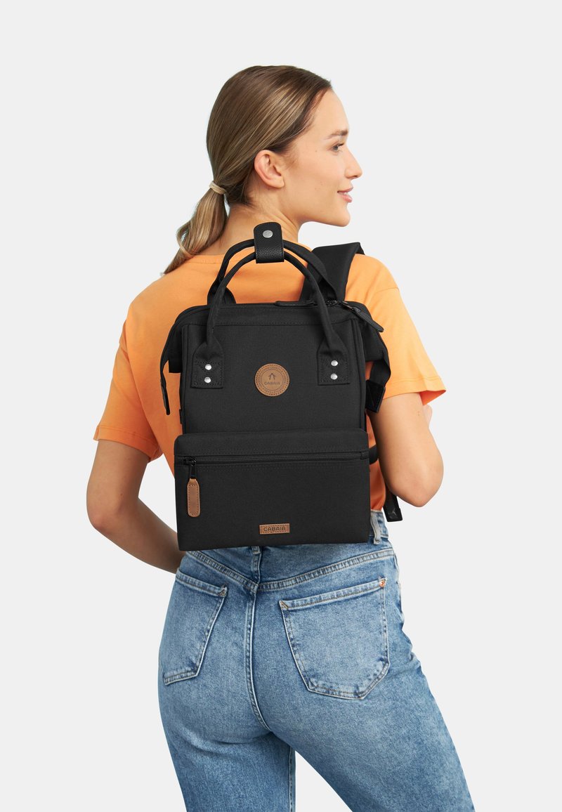 Sac à dos multifonction noir avec une poignée supérieure, des bretelles réglables, une poche zippée à l'avant et une surface texturée. Présente un détail de logo circulaire.