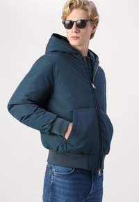 Chaqueta con capucha de color azul marino, con cierre de cremallera en la parte frontal, grandes bolsillos laterales, puños y dobladillo acanalados, fabricada con un tejido suave y duradero.