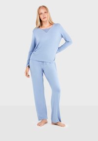 Ensemble de loungewear bleu clair composé d'un haut à manches longues avec un décolleté en V et des détails en dentelle, associé à un pantalon ample. Texture douce.