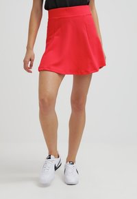 Rode skaterrok met een gestructureerd ontwerp, hoge tailleband en een uitlopende snit, gecombineerd met witte sneakers met zwarte accenten.