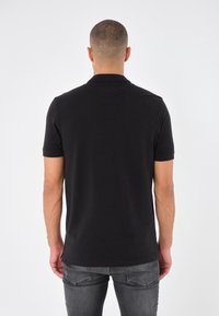 Černé polo tričko s krátkým rukávem a klasickým límcem, vyrobené z hladké bavlněné tkaniny. Design obsahuje rovný lem a jemné stehové detaily.