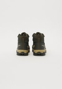 Ciemnooliwkowe buty trekkingowe z beżowymi akcentami, teksturowana cholewka i wzmocniony obcas. Posiadają wysoką cholewkę oraz trwałą gumową podeszwę.