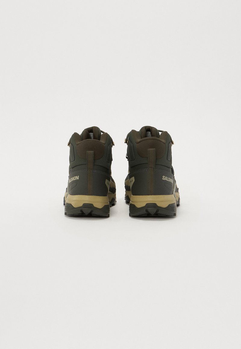 Dark olive green hiking boots with beige accents, textured upper, and reinforced heel. Features a high-top design and durable rubber outsole.