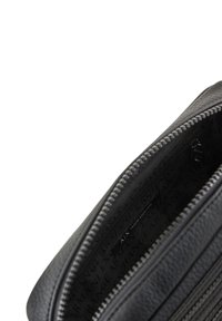 Borsa nera in pelle con zip superiore, dotata di una fodera interna e un logo. L'esterno presenta una finitura testurizzata e dettagli della zip lisci.