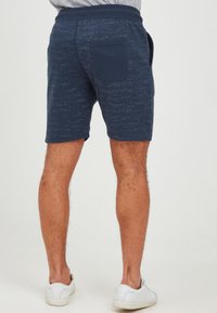 Marinblå shorts med ett texturerat mönster och elastisk midjeband, med en bakficka och en ledig passform, bärs med vita sneakers.