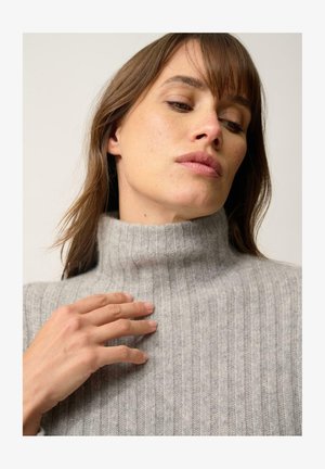 Lichtgrijze ribbelige coltrui gemaakt van zacht breimateriaal, met een hoge kraag en een gestructureerd patroon, met een close-up van de stof.