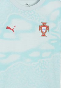 Maglia sportiva azzurro chiaro con logo Puma rosso sulla sinistra e stemma della squadra di calcio del Portogallo sul petto a destra.