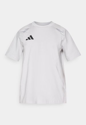 Λευκό βαμβακερό μπλουζάκι με μαύρο λογότυπο Adidas στο αριστερό μέρος του στήθους, κοντά μανίκια, στρογγυλή λαιμόκοψη και απαλό ύφασμα. Διαθέτει ράγκλαν ώμους.