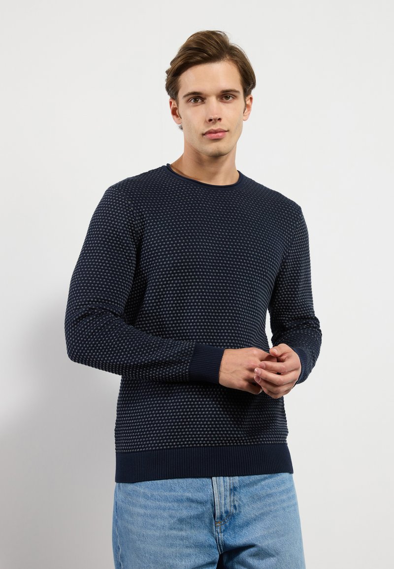 Navy blue textured sweater with a raised dot pattern, ribbed cuffs, and hem. Crew neck design, made from a soft fabric.