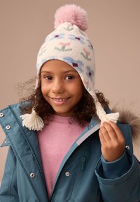 Gestrickte Wintermütze in Creme mit floralen Mustern in Blau, Pink und Grün. Mit rosa Bommel und weißen Quasten an den Ohrenschutzklappen.