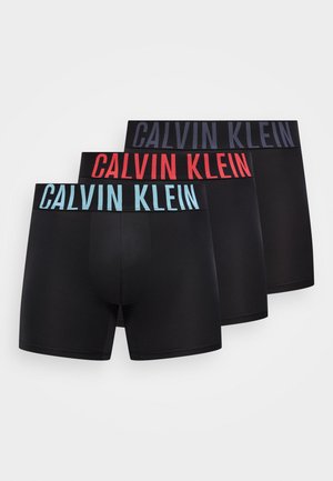 Tres pares de calzoncillos bóxer negros con logotipos de Calvin Klein en las bandas de la cintura en azul, rojo y gris oscuro, dispuestos superpuestos.