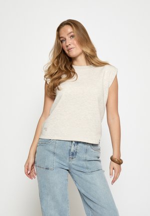 Jasnobeżowy, bezrękawnik z okrągłym dekoltem, lekko opuszczonymi pachami i subtelną fakturą. Dopasowany do luźnych, niebieskich dżinsów.