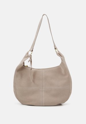 Sac à épaule en daim beige avec une fermeture éclair, une bandoulière simple et des anneaux métalliques dorés reliant la bandoulière au corps du sac.