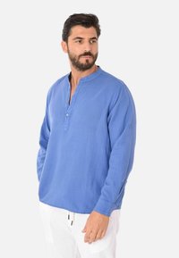 Camicia a maniche lunghe in lino azzurro chiaro con colletto alla cinese, dettagli con bottoni e vestibilità comoda. Presenta una texture sottile e un orlo dritto.
