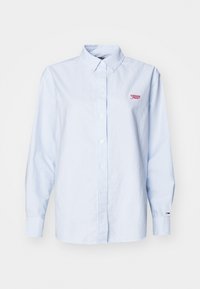 Lyseblå skjorte med knapper laget av bomull, med lange ermer og en liten rød brodert logo på brystet. Enkel design, klassisk passform.