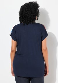 Camiseta de manga corta azul marino con un corte holgado, con acentos de colores brillantes en los hombros y una textura suave y lisa.