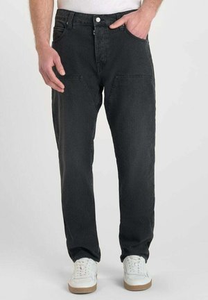 Jean en denim noir avec une coupe droite, présentant des poches avant et une finition texturée. Porté avec des baskets blanches.