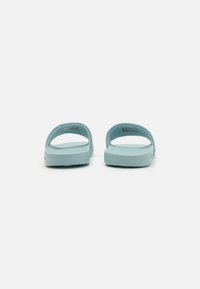 Des sandales à glissière bleu clair en caoutchouc souple, avec une semelle plate, un dos ouvert et un design à double sangle pour un enfilage facile.
