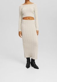 Kremowy krótki sweter w sploty warkoczowe i pasująca spódnica midi, z prążkowanymi mankietami i talią, w zestawieniu z czarnymi, szpiczastymi botkami na kostkę.