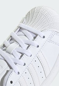 Bijela tenisica s teksturiranim sintetičkim gornjim dijelom, jednobojnim vezicama, prošivenim detaljima i uzorkovanim vrhom za prstima radi boljeg prianjanja.