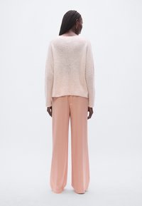 Rosa gestrickter Pullover mit lockerem Sitz und geripptem Saum, kombiniert mit weiten rosa Hosen. Weiche Textur, minimalistisches Design, keine Muster.