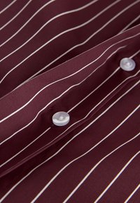 Bordó ing fehér, függőleges csíkokkal; pamut anyag; két fehér gombbal díszítve; sima textúra; hajtókás gallér és patent részlet.