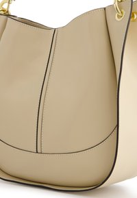 Beige leather handbag featuring a smooth finish, curved silhouette, contrasting black stitching, and gold hardware accents.