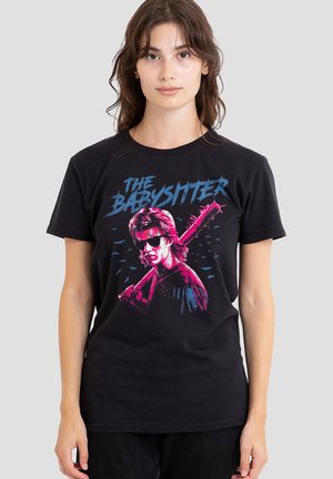 Young woman wearing black T-shirt with "The Babysitter" text and graphic of person holding spiked bat in neon pink and blue colors.
