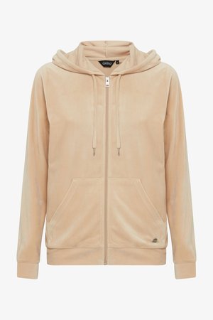 Beige zip-up hoodie in soft, textured fabric. Features a drawstring hood and front pockets. Zipper and logo detail at the hem.