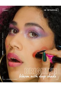 NYX sminkprodukt applicerad på kinden, med rosa och röda nyanser. Modellen har lockigt hår, djärv ögonmakeup med lila toner och livfulla läppar.