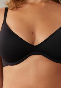 Zwarte bh met naadloze cups, een V-vormige halslijn, verstelbare bandjes en een haaksluiting. Glad materiaal met een matte afwerking.