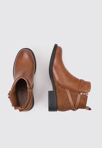 Botines marrones hasta el tobillo fabricados con material sintético, con cierre lateral, panel texturizado y tacón apilado negro. Acabado liso con detalles de costura.