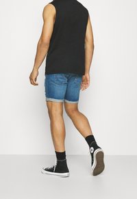 Shorts de mezclilla en un lavado azul claro con bordes deshilachados, combinados con una camiseta sin mangas negra y zapatillas altas de lona negras.