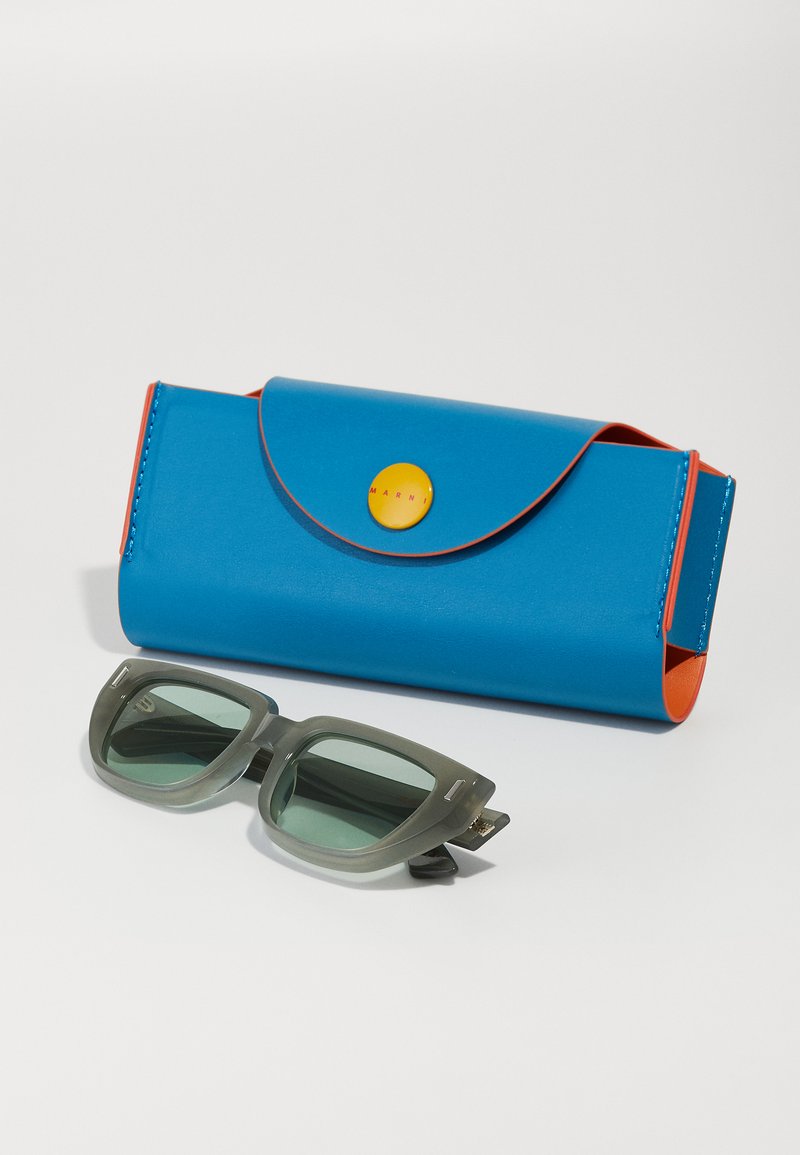 Sonnenbrille mit grünen Gläsern, grauem Rahmen. Blaues und oranges rechteckiges Etui mit einem gelben Druckknopfverschluss. Glatte, glänzende Oberflächen.