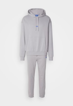 Grå hoodie och matchande sweatpants gjorda av mjukt material. Hoodien har en framficka och en dragkedja i huvan, accentuerad med en blå logotyp.