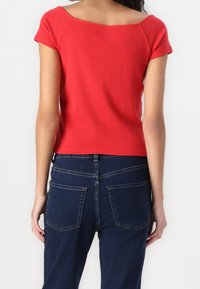 Červený bavlněný top s krátkým rukávem a širokým výstřihem, spárovaný s tmavě modrými denimovými džínami s dvěma zadními kapsami a klasickým střihem.