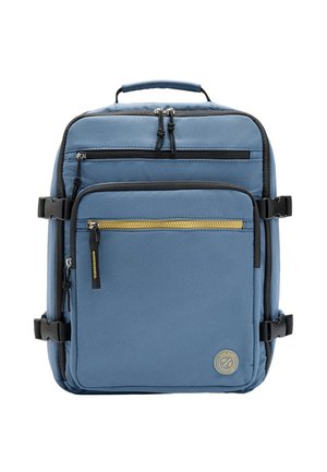 Niebieski prostokątny plecak z kilkoma komorami na zamki błyskawiczne, czarne klamry po bokach oraz okrągła naszywka z logo na przedniej kieszeni.